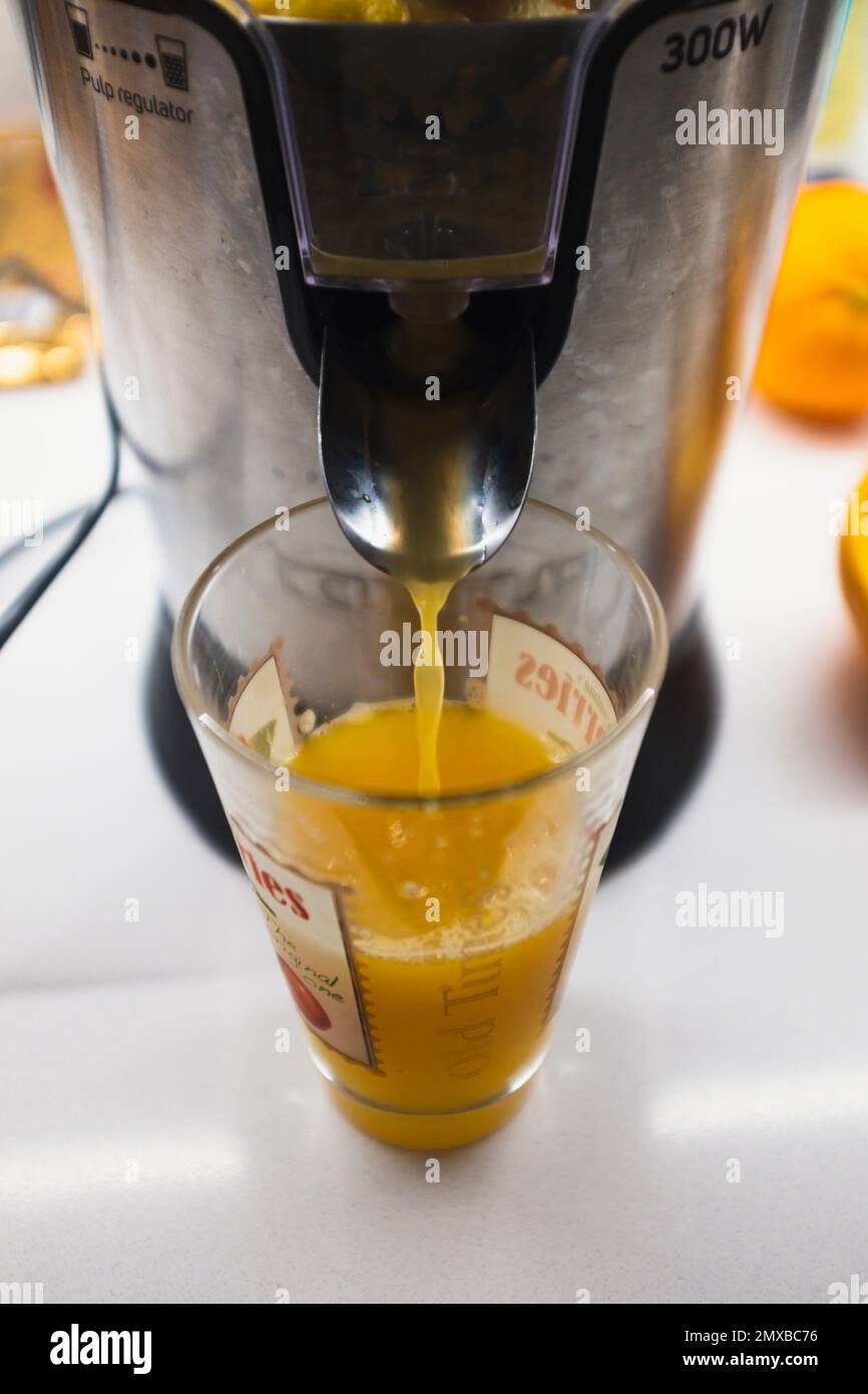 Orange juice machine pouring liquid juice in a drinking glass on a