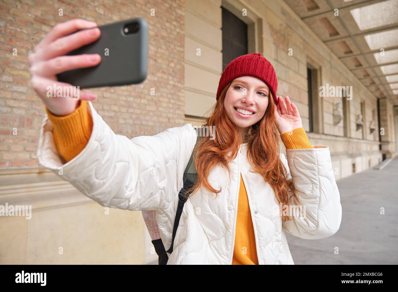 Stylish redhead girl tourist, takes selfie in front of tourism attraction,  makes photo with smartphone, looks at mobile camera and poses 35118543  Stock Photo at Vecteezy