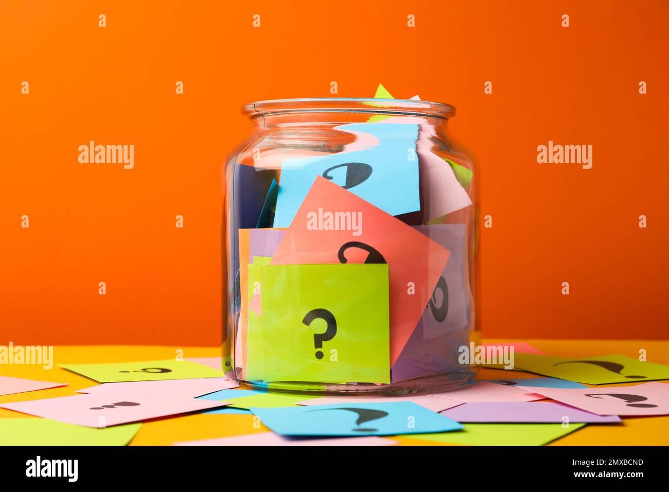 Colorful cards with question marks in glass jar on orange background