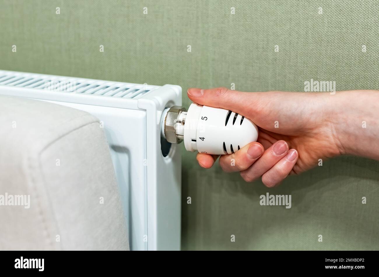 Hand turning on heat with valve knob of home radiator, adjusting indoor