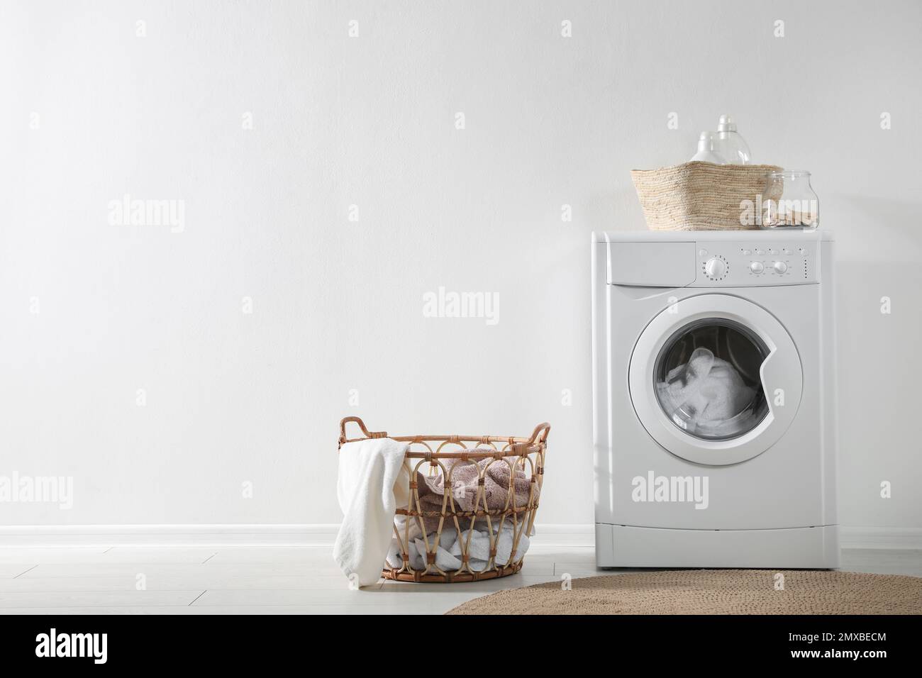 Modern washing machine and laundry baskets near white wall indoors