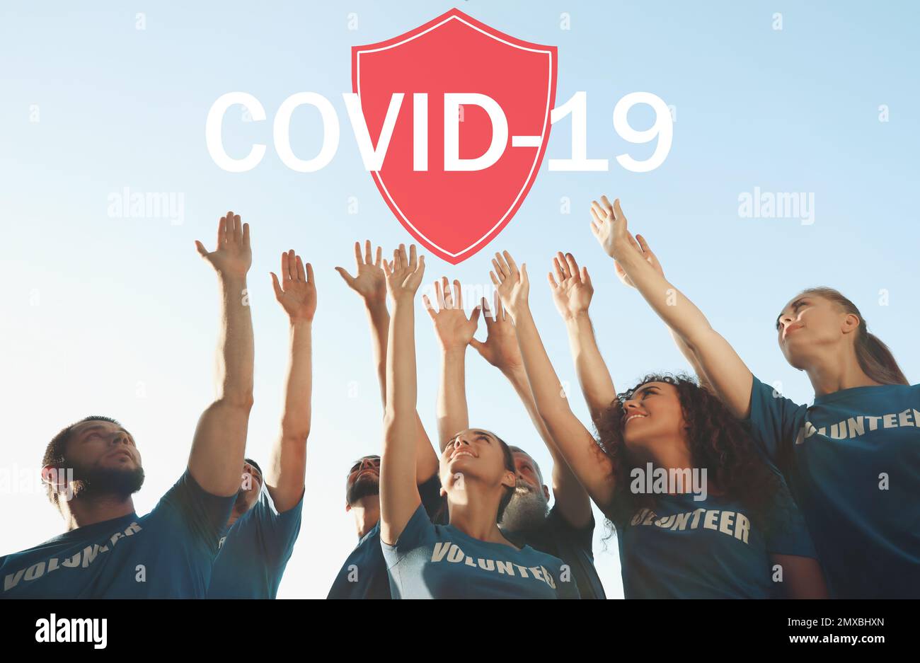 Volunteers uniting to help during COVID-19 outbreak. Group of people raising hands outdoors, shield illustration Stock Photo