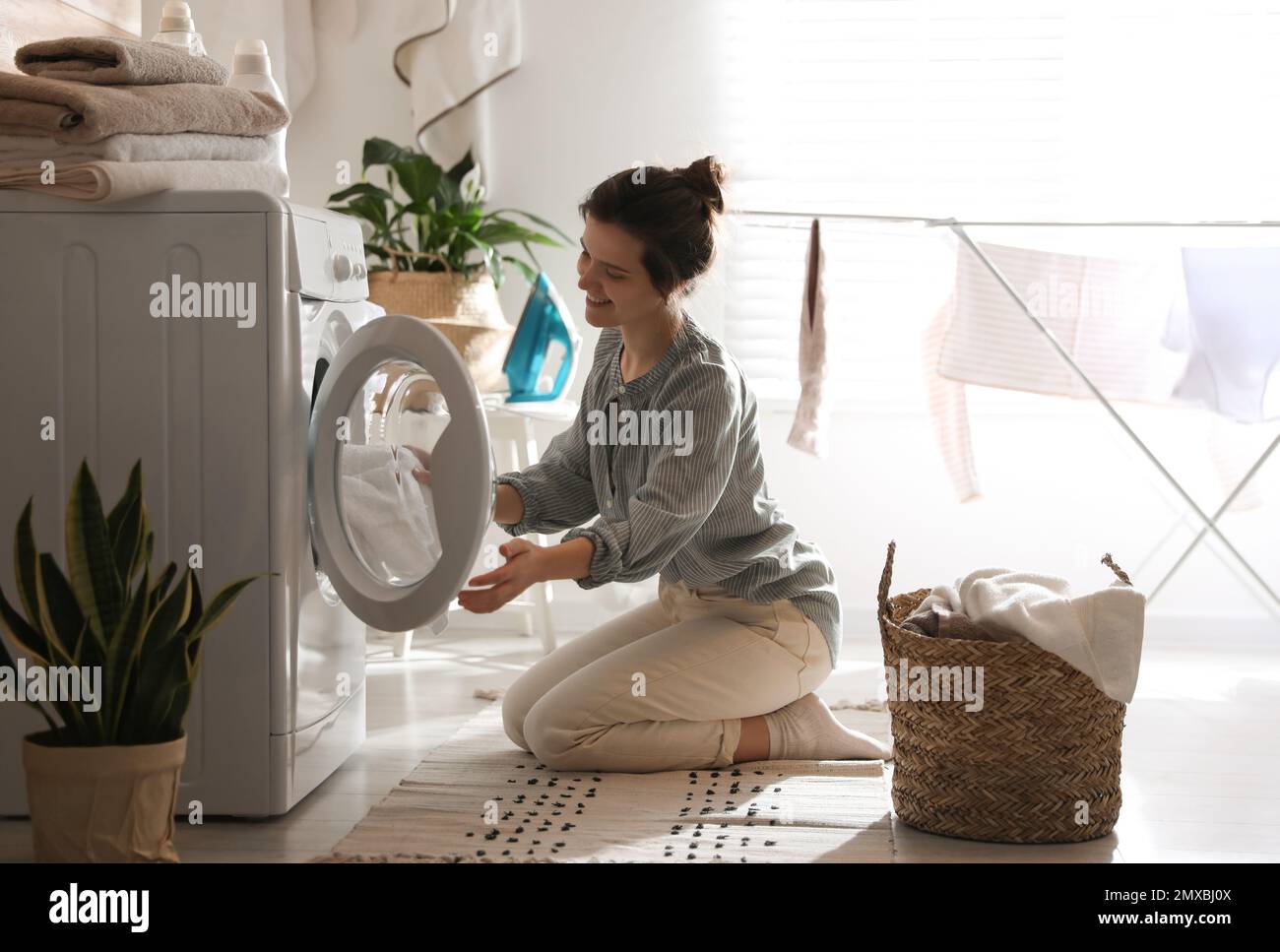 Young woman taking laundry out of washing machine at home Stock Photo