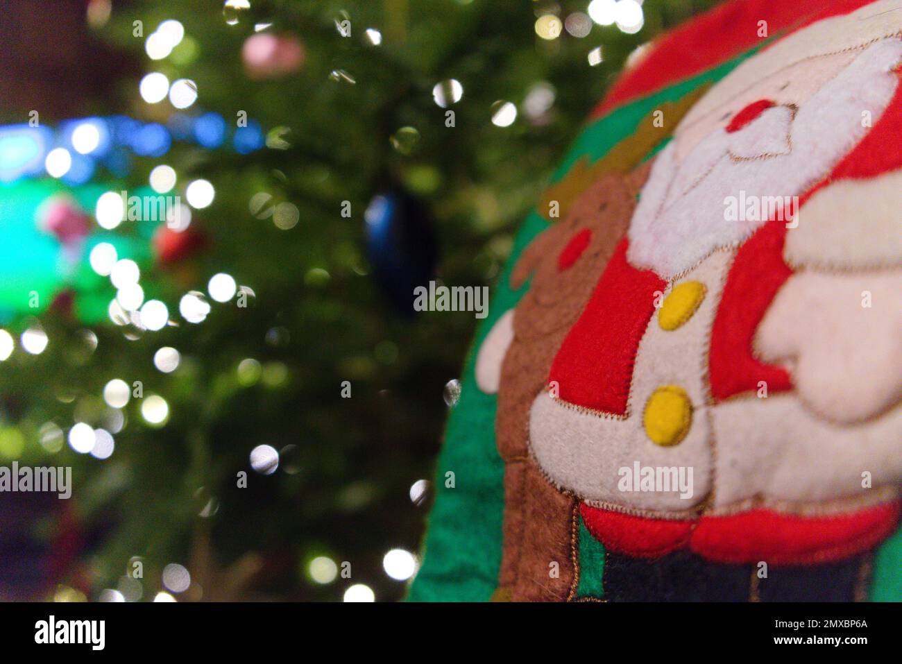 Stocking with Santa Clause and reindeer in foreground, Christmas tree with red, blue and pink baubles and lights in midground and television behind Stock Photo