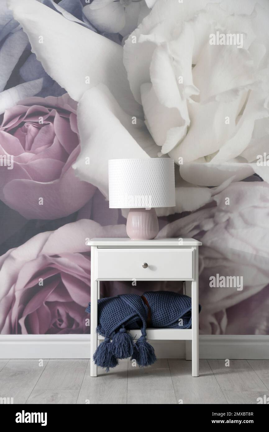 White nightstand near wall with floral wallpaper. Stylish room interior
