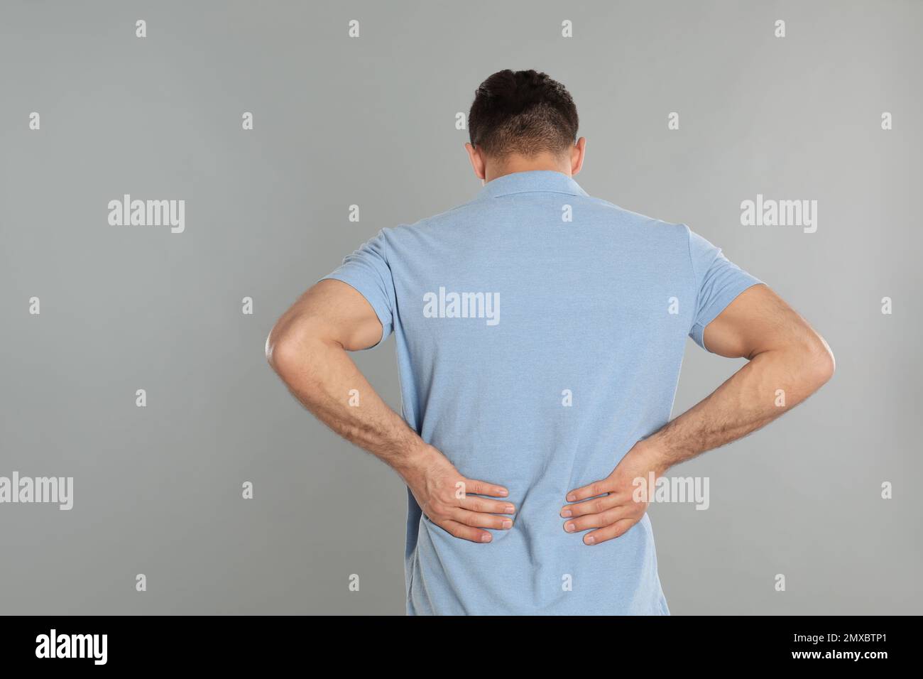 Man suffering from lower back pain on light grey background. Visiting