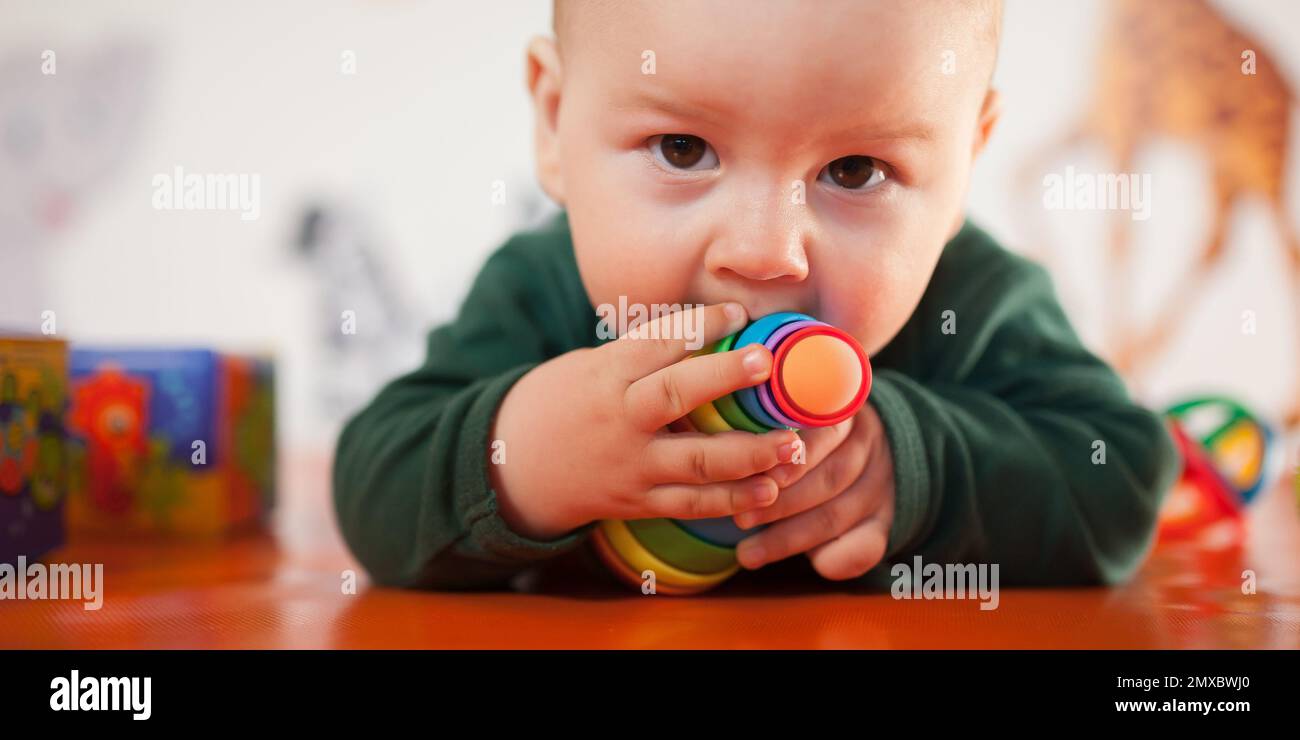 Cute baby boy nibbles and eats colourful toys because her small new