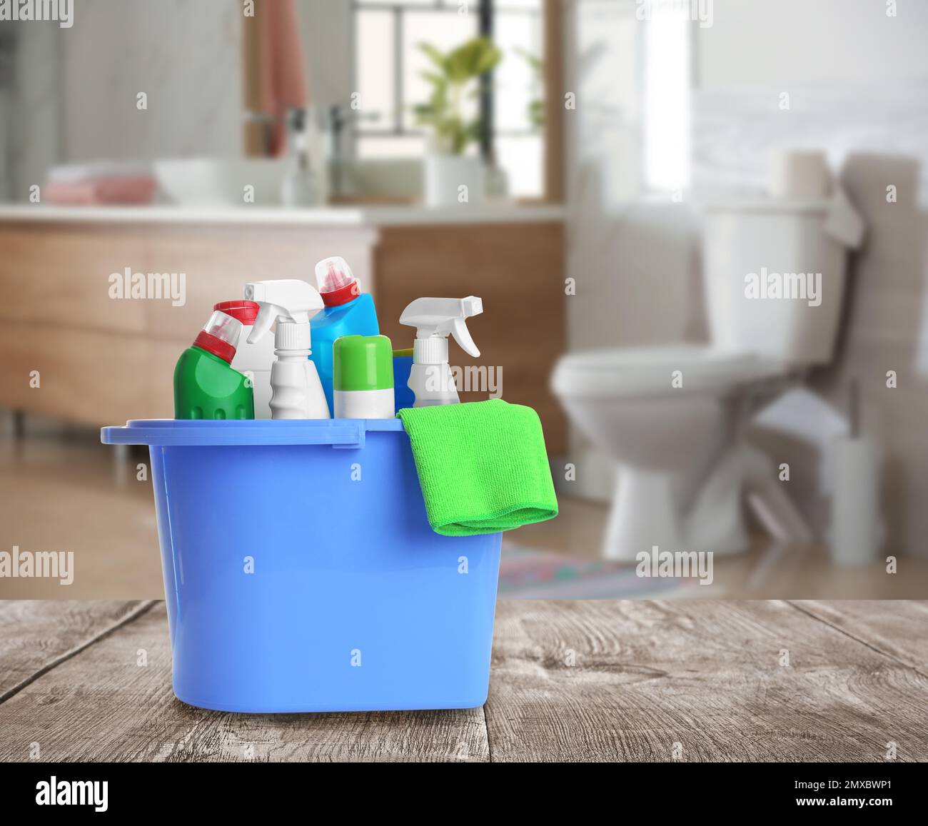 Bucket with cleaning supplies on wooden table in bathroom Stock Photo