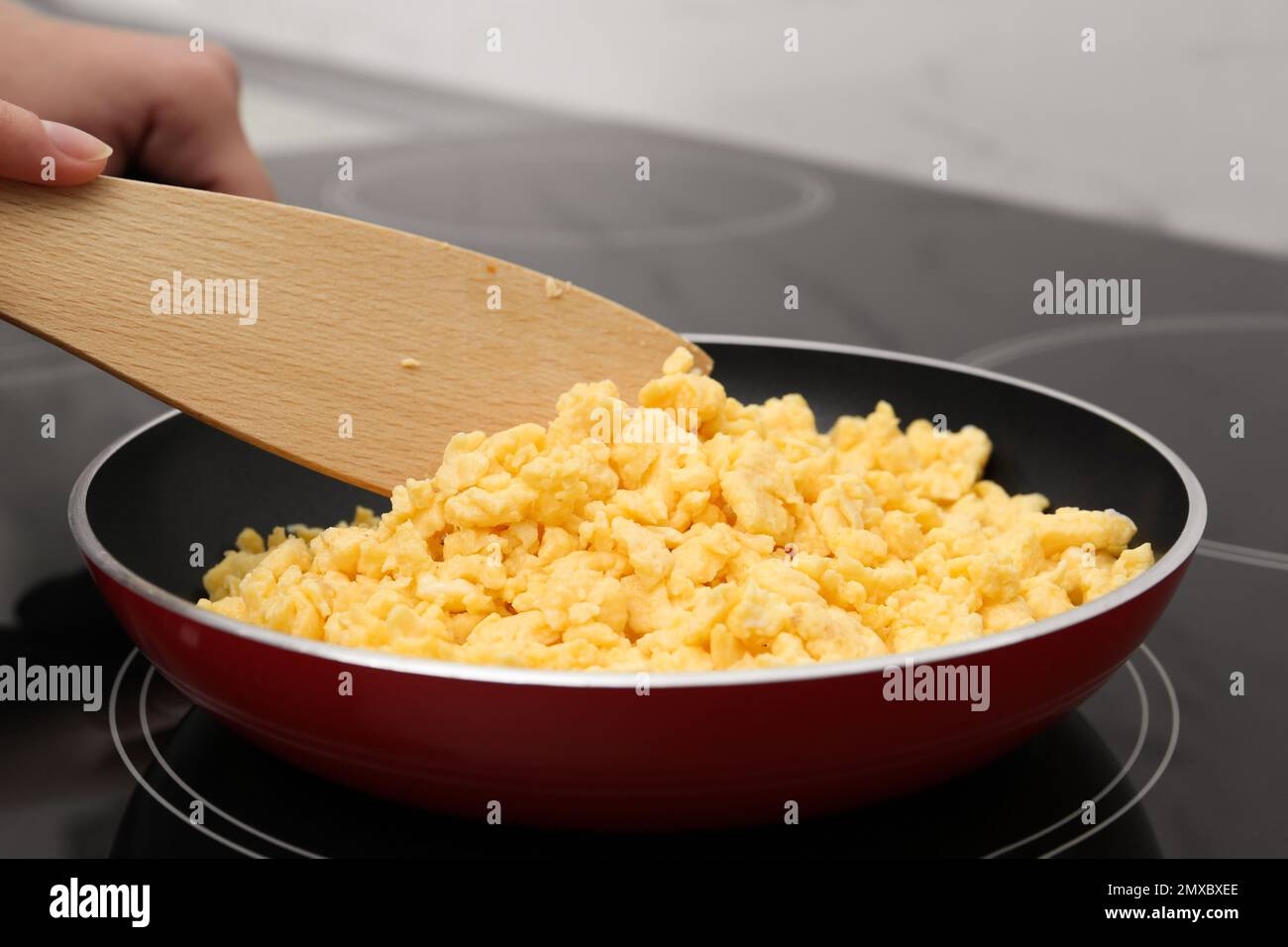 Woman cooking tasty scrambled eggs in frying pan on stove, closeup