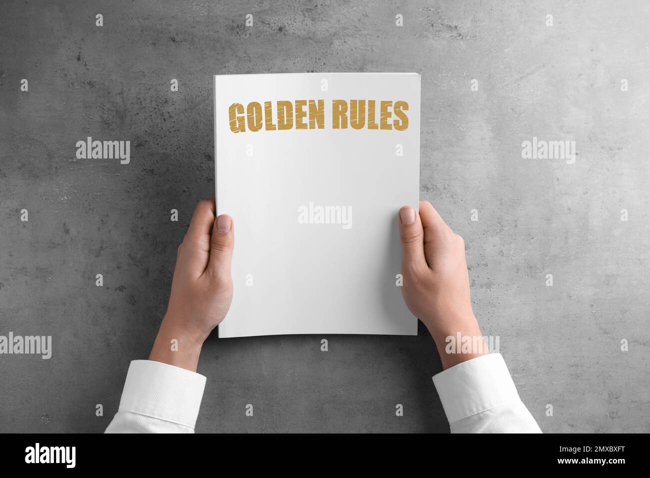 Man holding booklet with phrase GOLDEN RULES at grey table, top view Stock Photo