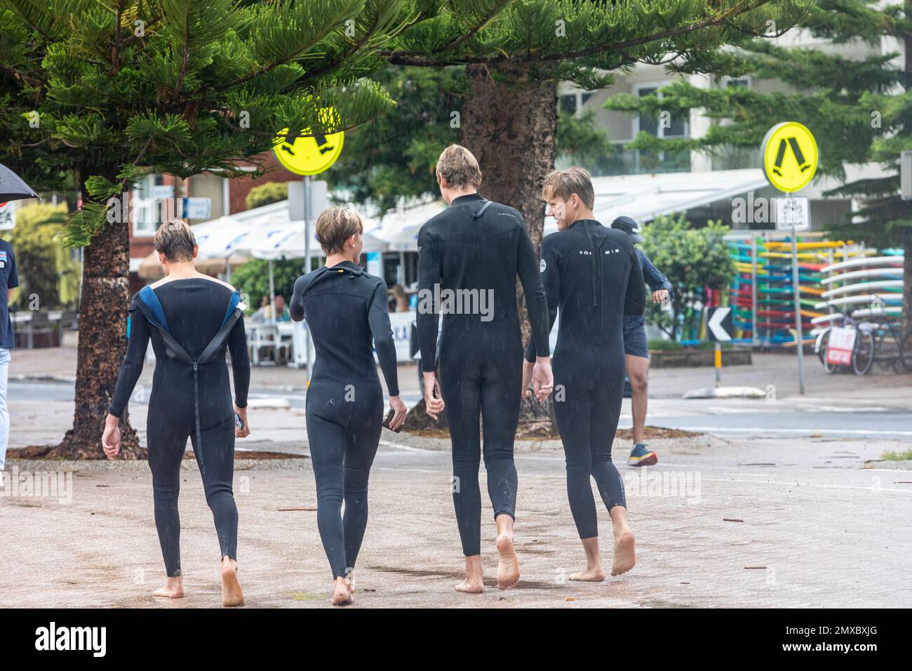Four young teenage boys wearing wetsuits walking along the promenade in