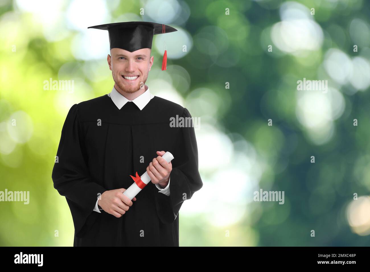 Happy student with graduation hat and diploma on blurred background ...
