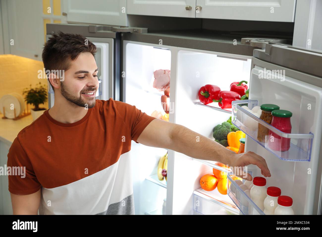 Young man taking yoghurt out of refrigerator indoors Stock Photo Alamy