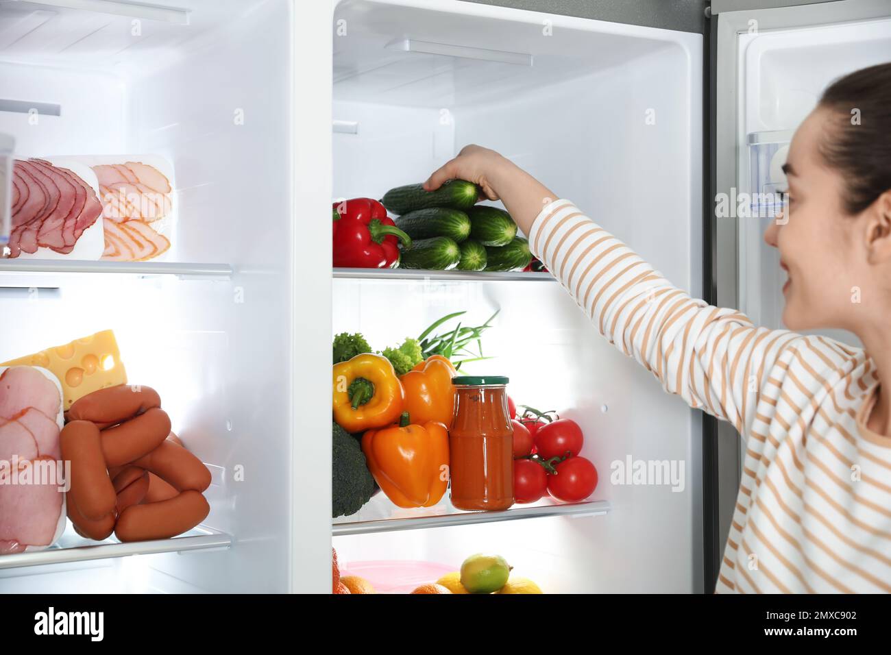 Young woman taking cucumber out of refrigerator, closeup Stock Photo