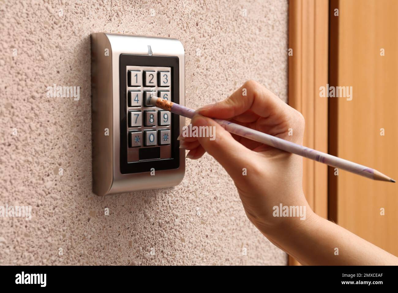 Woman using pencil to enter code on electronic lock's keypad indoors, closeup Stock Photo