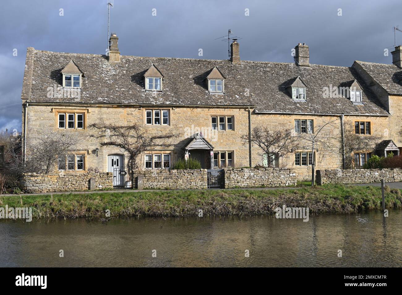 A row of houses on the bank of the River Eye in the Cotswold village of Lower Slaughter Stock Photo