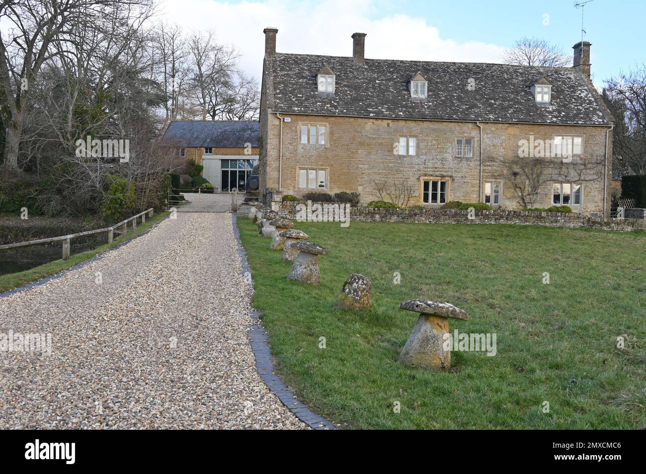 College Farm in the Cotswold village of Wyck Rissington, Gloucestershire has row of staddle stones as an ornamental decoration beside the driveway. Stock Photo