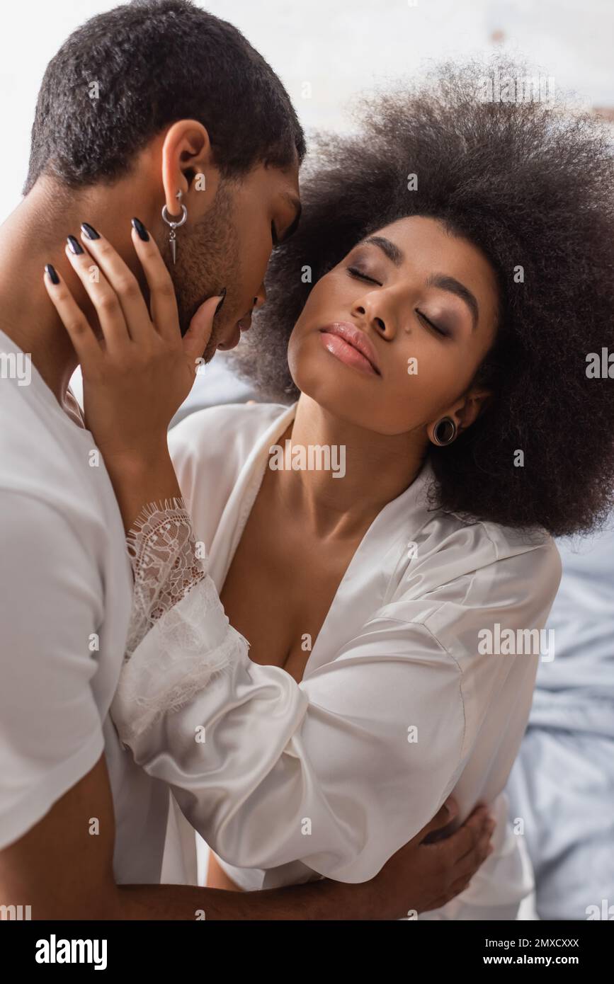 hot african american woman in white silk robe hugging with young boyfriend in bedroom Stock Photo