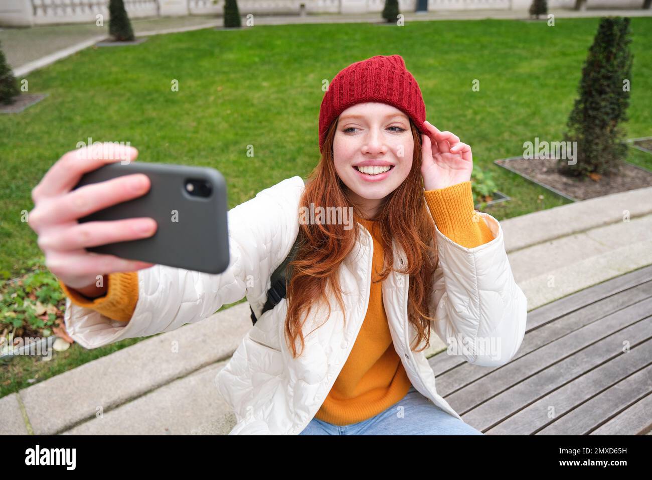 Beautiful young urban girl takes selfie on smartphone, relaxed on bench ...