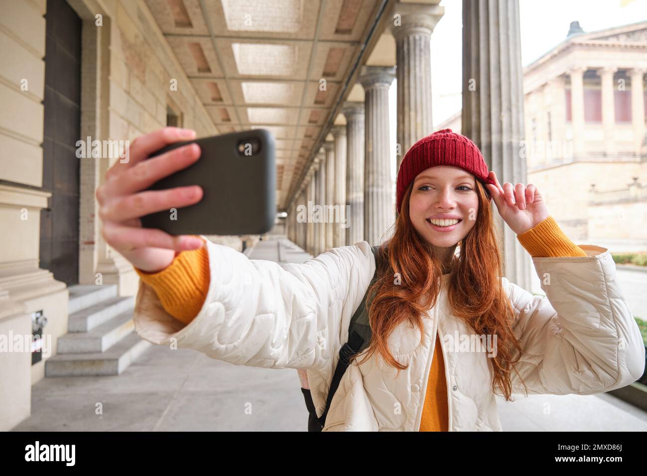 Cute young redhead woman takes selfie on street with mobile phone, makes a photo of herself with smartphone app on street. Stock Photo