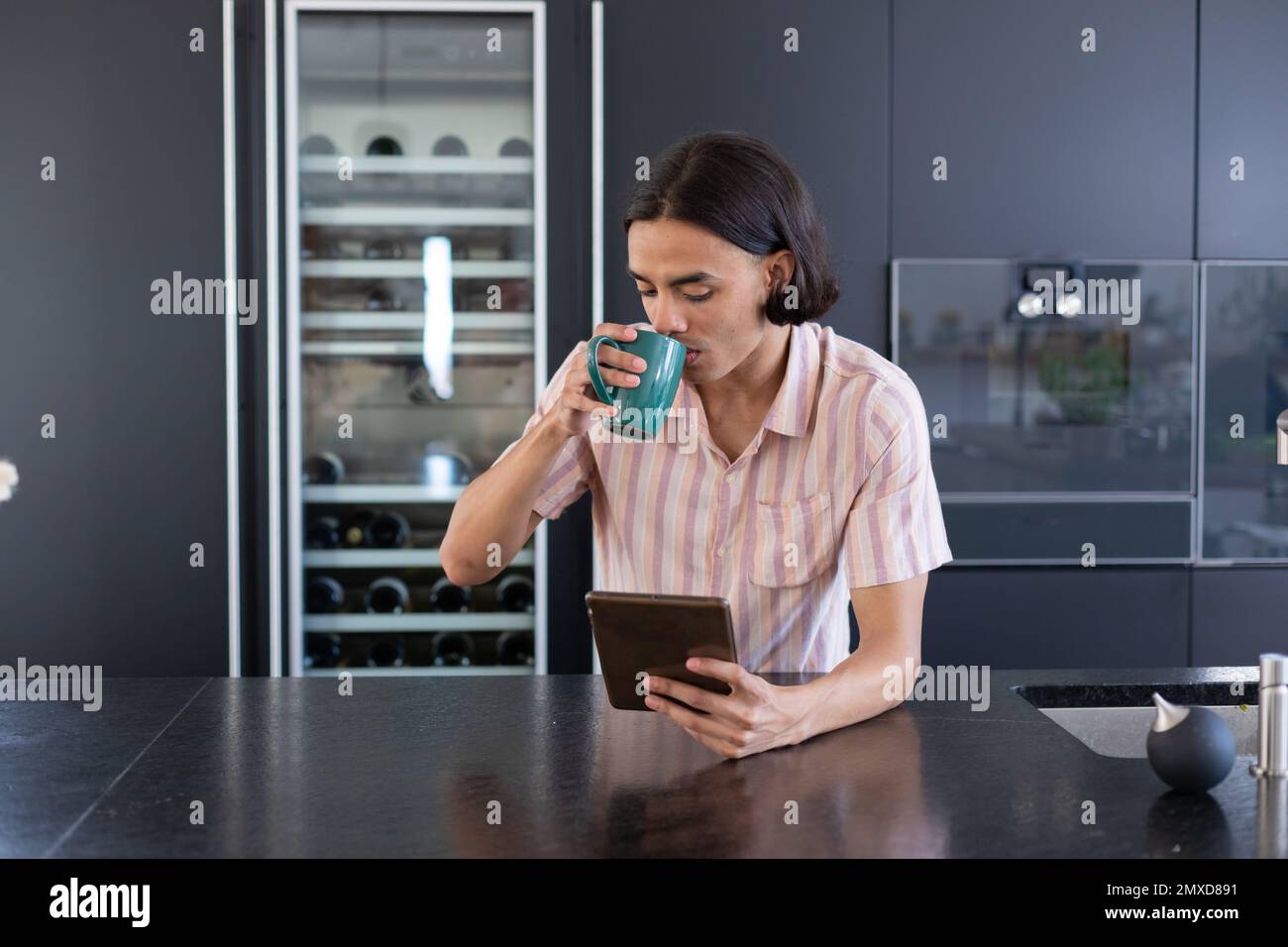 Happy biracial man using tablet and drinking coffee in kitchen Stock Photo
