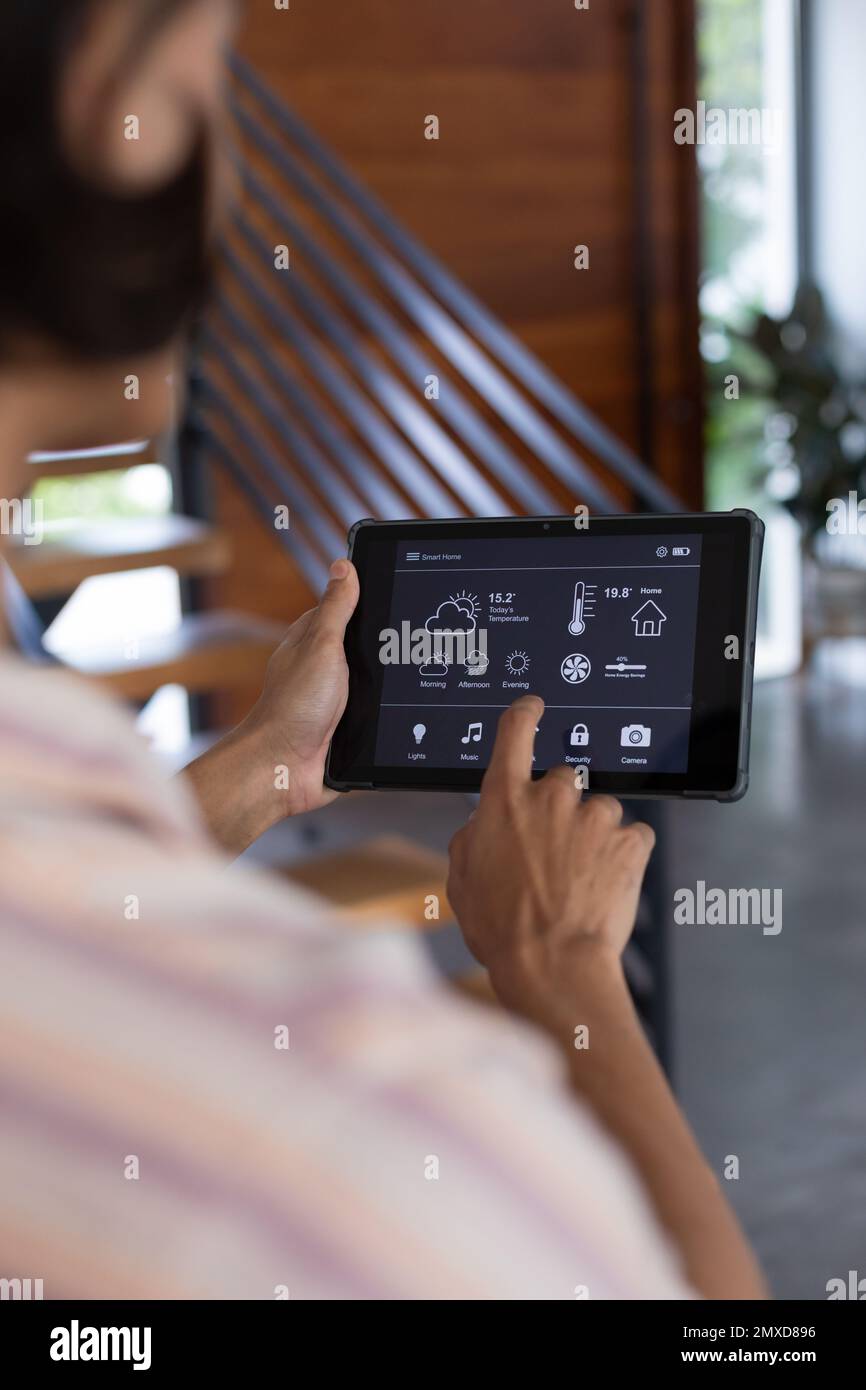 Vertical of hands of biracial man at home using tablet with smart home ...