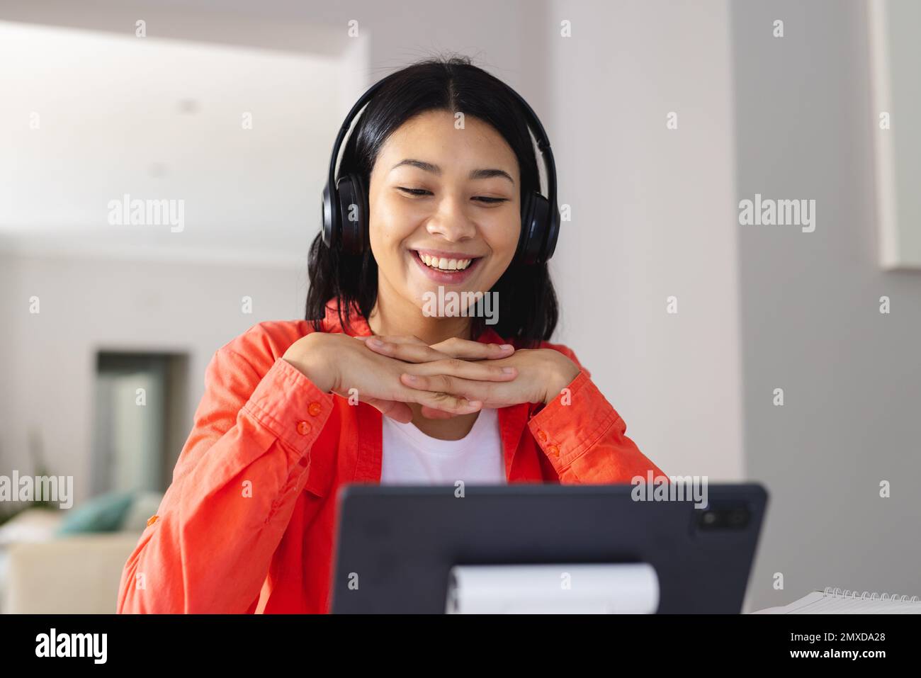 Image of biracial woman in headphones smiling during video call on tablet at home, copy space. Working from home, technology, communication and lifest Stock Photo