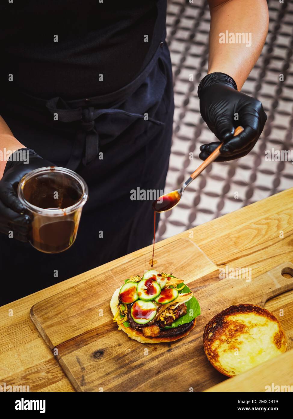 cook hands dripping teriyaki sauce on a fresh made tasty burger in a kitchen Stock Photo