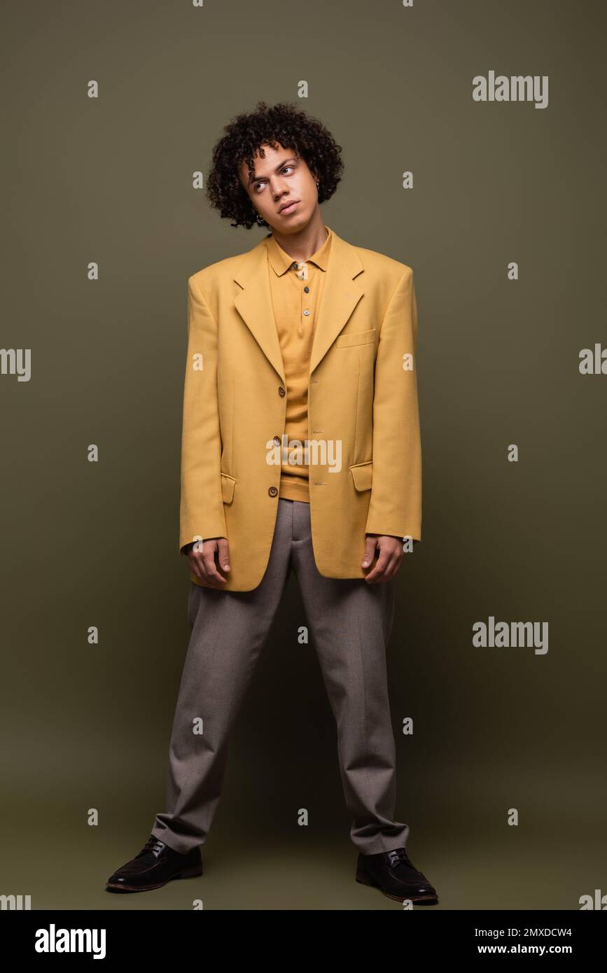 full length of young african american guy in yellow jacket and pants standing on olive grey background,stock image Stock Photo