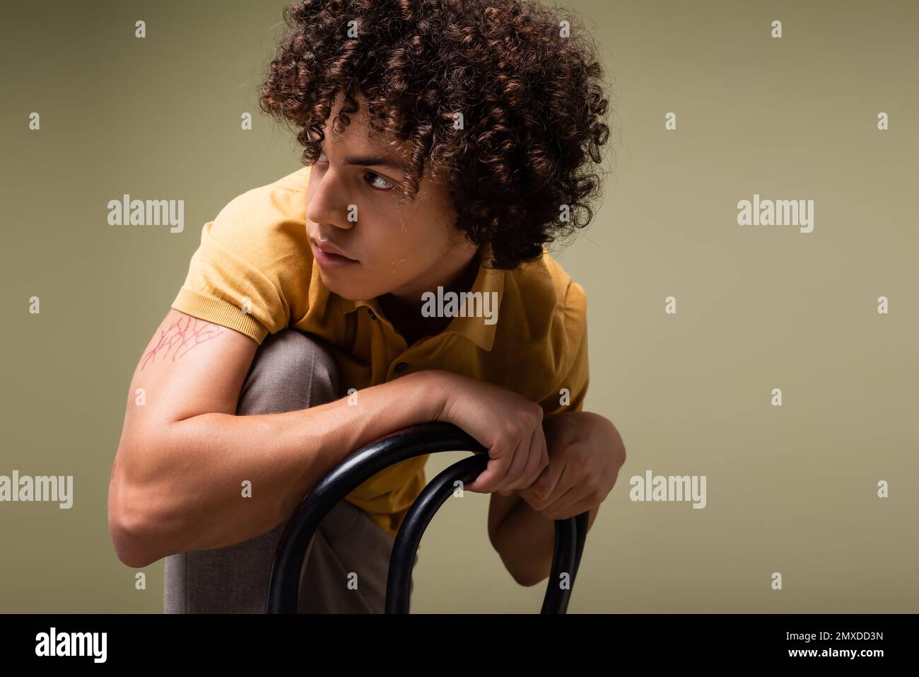 stylish african american man with curly hair looking away while posing near chair isolated on grey,stock image Stock Photo
