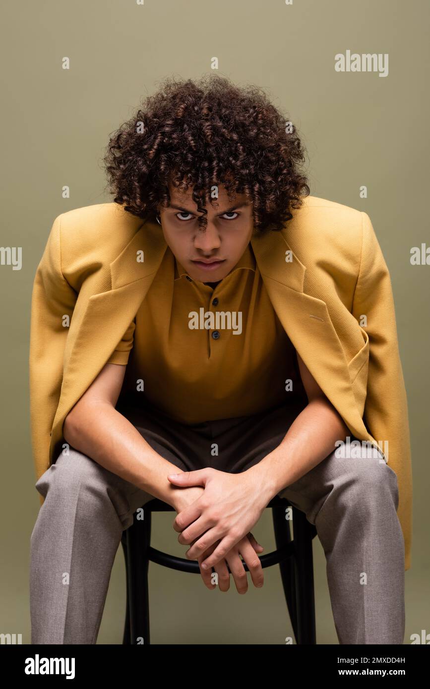 young and confident african american man in yellow jacket looking at camera while sitting isolated on grey,stock image Stock Photo