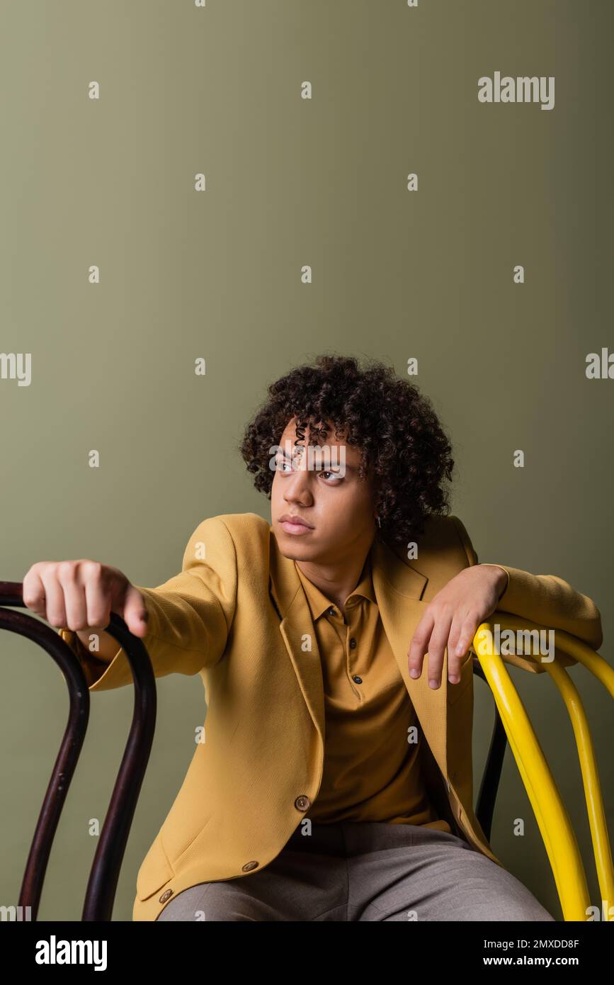 stylish african american man in yellow blazer looking away near black and yellow chairs isolated on grey,stock image Stock Photo