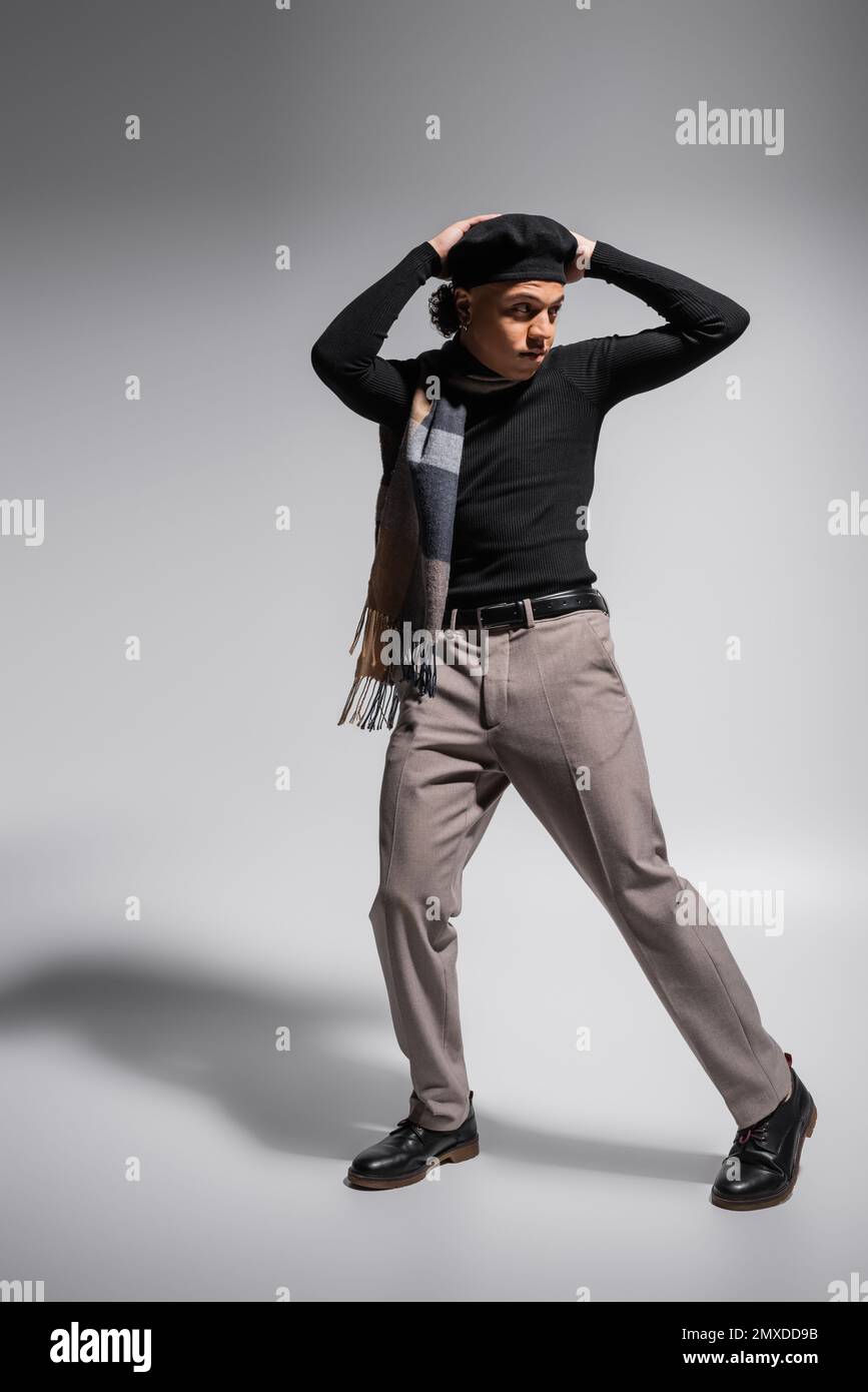 full length of young and trendy african american man in black pullover and plaid scarf posing with hands above head on grey background,stock image Stock Photo
