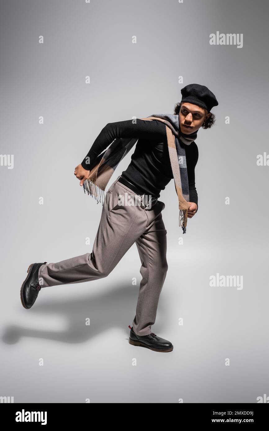 full length of african american man in black beret and sweater with trousers running and looking away on grey background,stock image Stock Photo