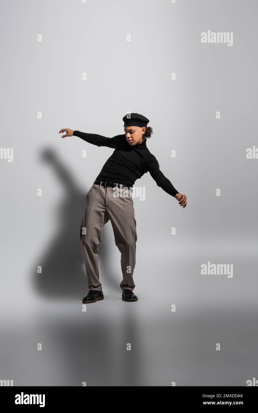full length of young and stylish african american guy in black beret and turtleneck with pants posing on grey background,stock image Stock Photo