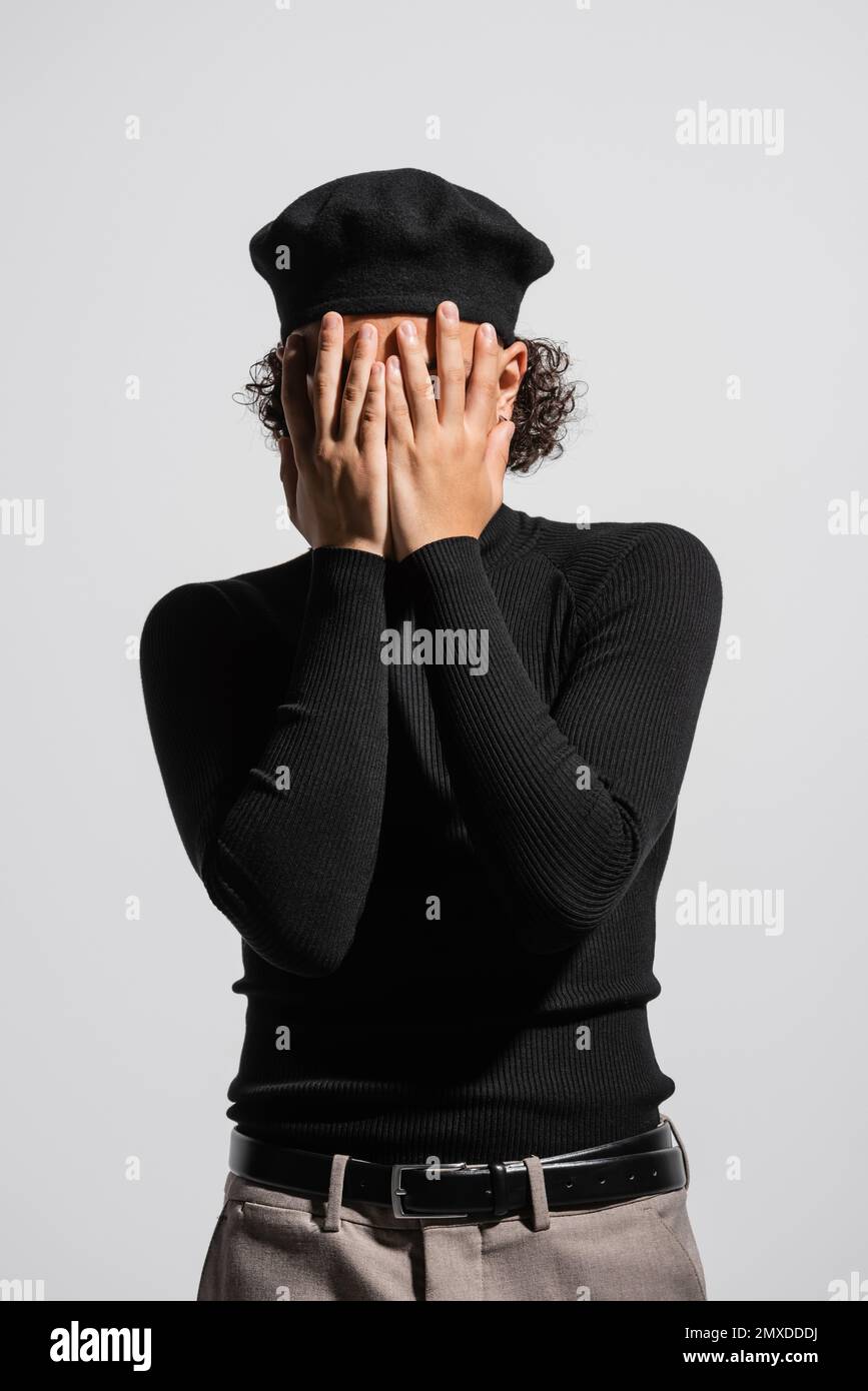 young african american man in stylish beret and black turtleneck covering face with hands isolated on grey,stock image Stock Photo