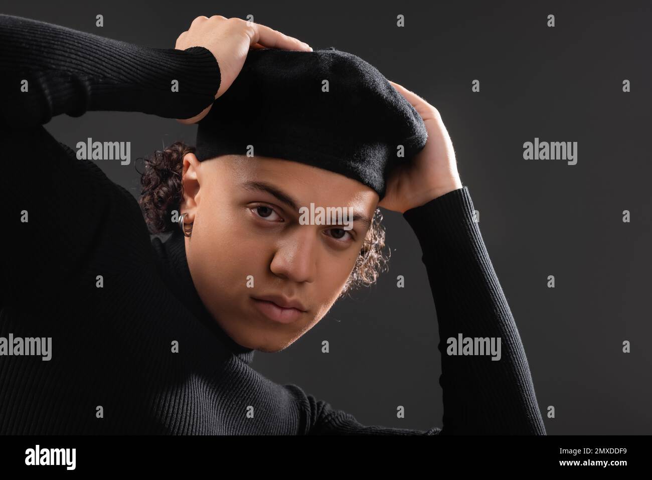 young and trendy african american man in black turtleneck adjusting beret and looking at camera isolated on dark grey,stock image Stock Photo