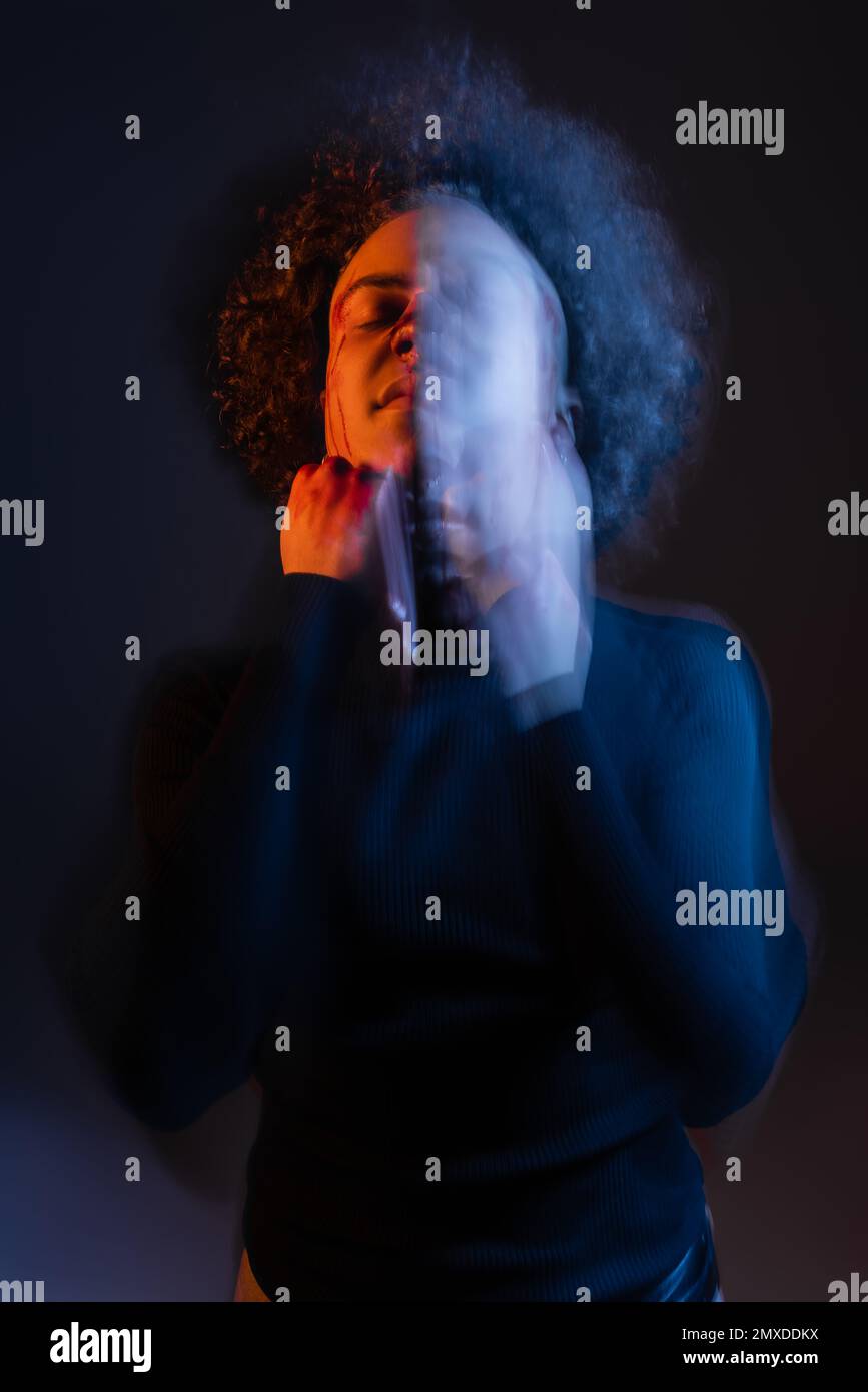 double exposure of wounded african american man with bloody face standing with closed eyes on black with red and blue light,stock image Stock Photo