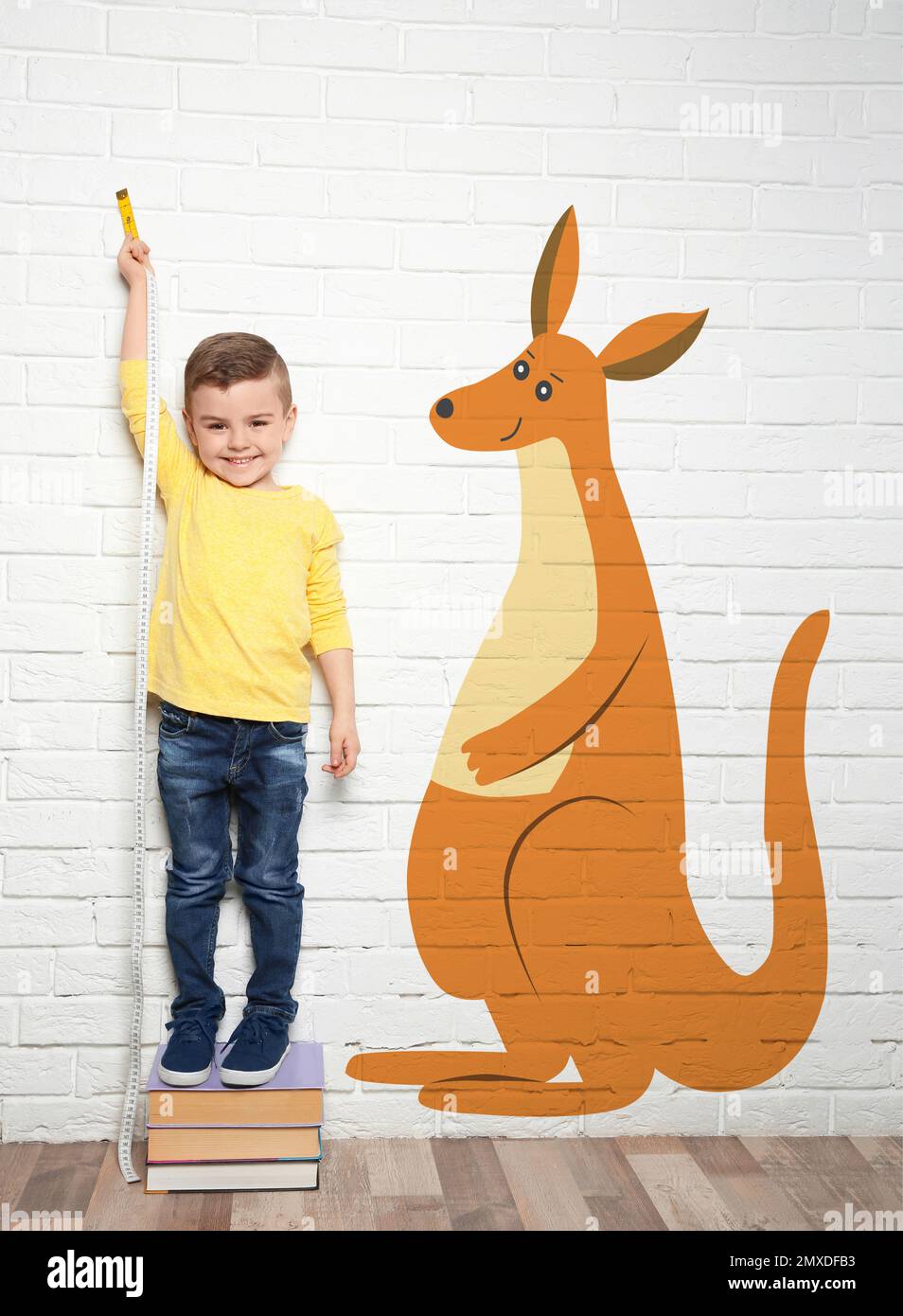 Little boy measuring height and drawing of kangaroo near white brick wall Stock Photo