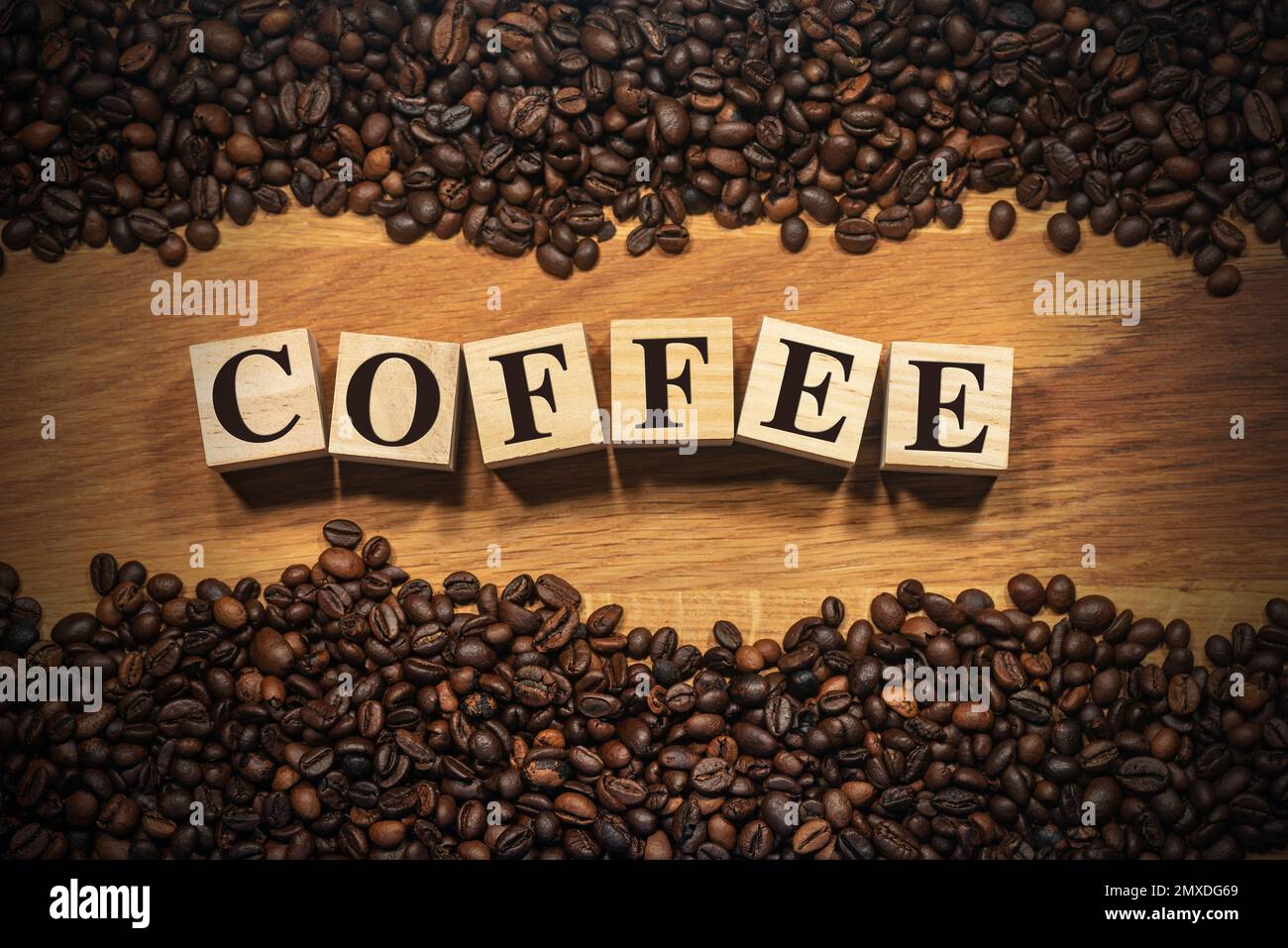 Large group of roasted coffee beans on a wooden background and the text Coffee, made of wooden blocks. Photography. Stock Photo