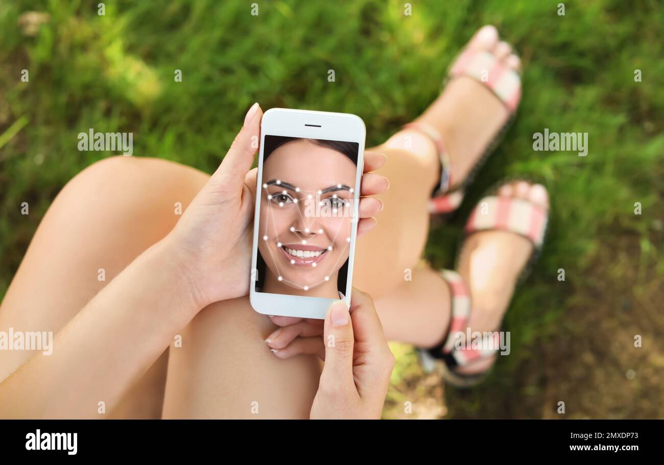 Woman using smartphone with facial recognition system outdoors, closeup. Biometric verification Stock Photo