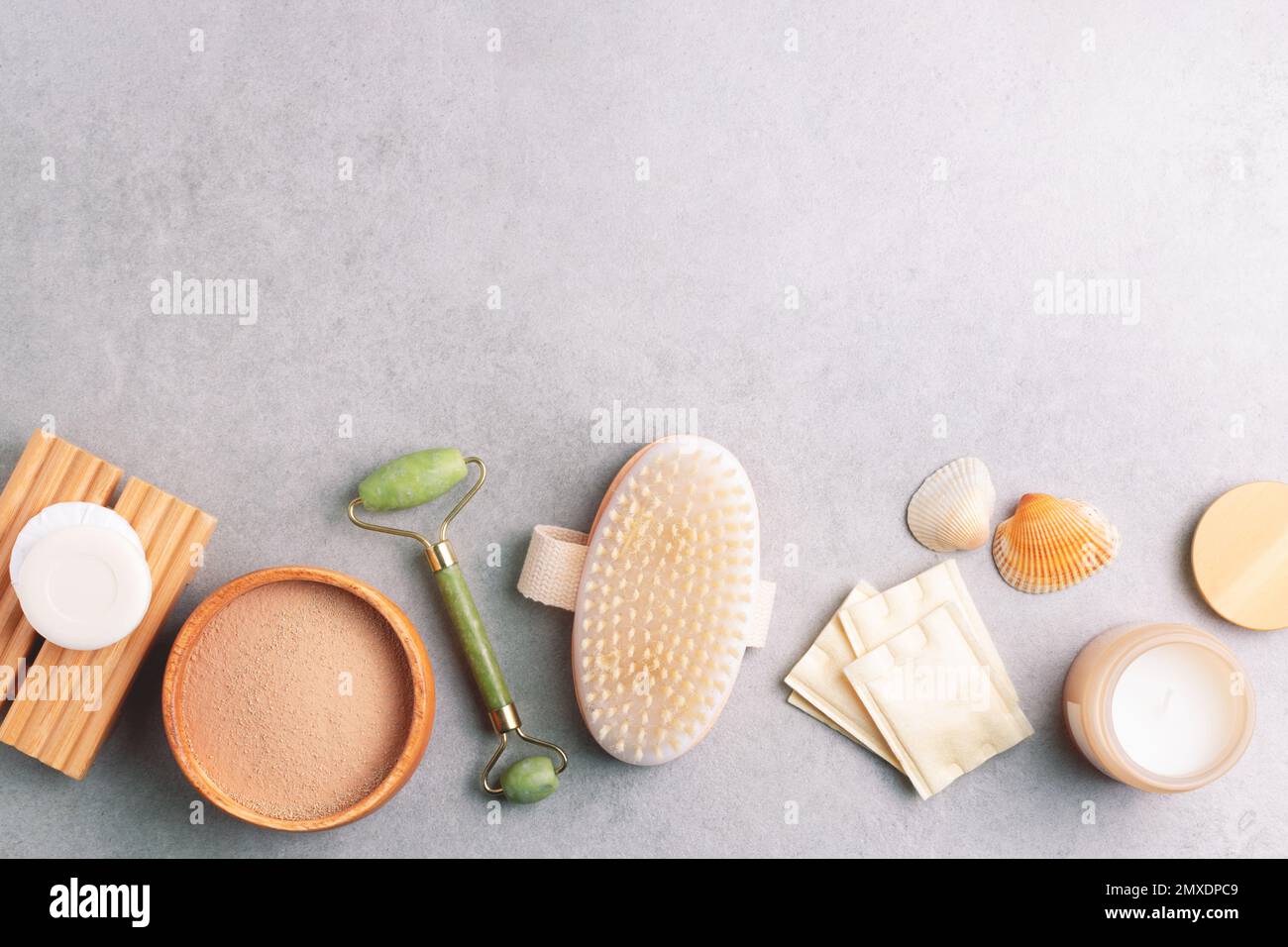 Set of skin care and wellness products. Massage brush, jade roller, cotton pads, soap, facial clay mask on grey stone background. Stock Photo