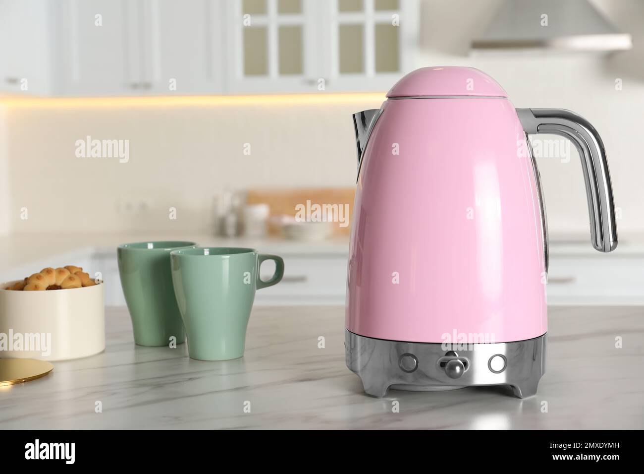 Modern electric kettle, cups and cookies on table in kitchen Stock Photo -  Alamy