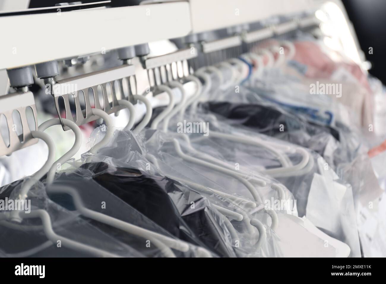 Hangers with clothes on garment conveyor at drycleaner's, closeup