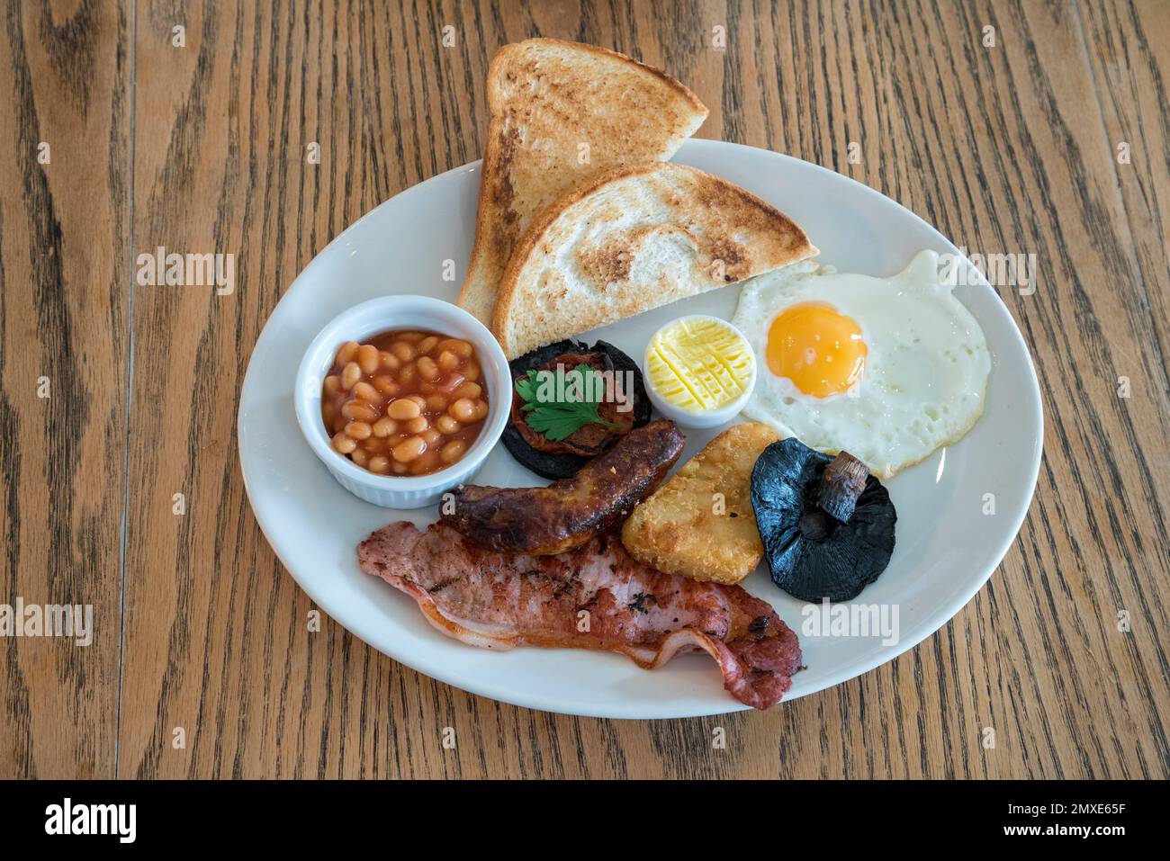 Full english fried breakfast served on a white plate on a cafe table - point of view Stock Photo