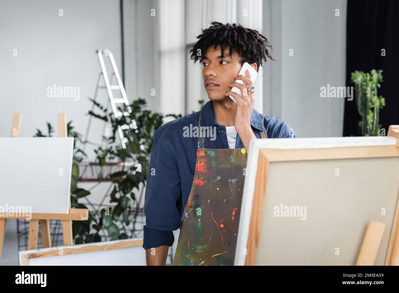 Young african american artist in apron talking on cellphone in workshop,stock image Stock Photo