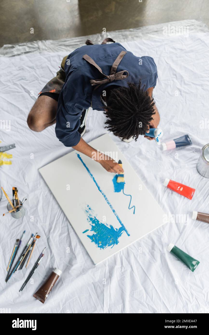 Overhead view of african american artist painting on canvas on floor in studio,stock image Stock Photo