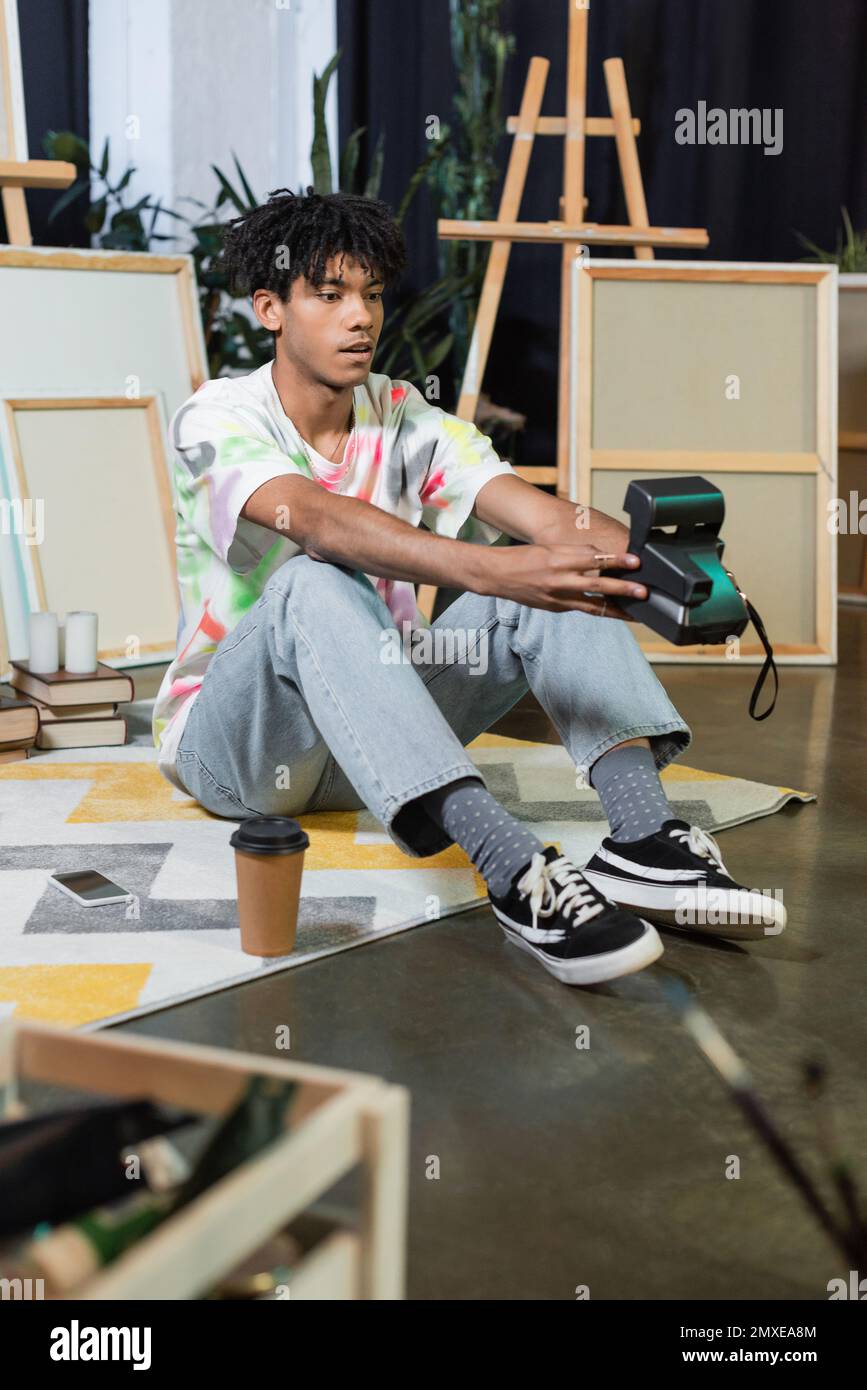 Young african american artist taking selfie on vintage camera near coffee and smartphone in studio,stock image Stock Photo