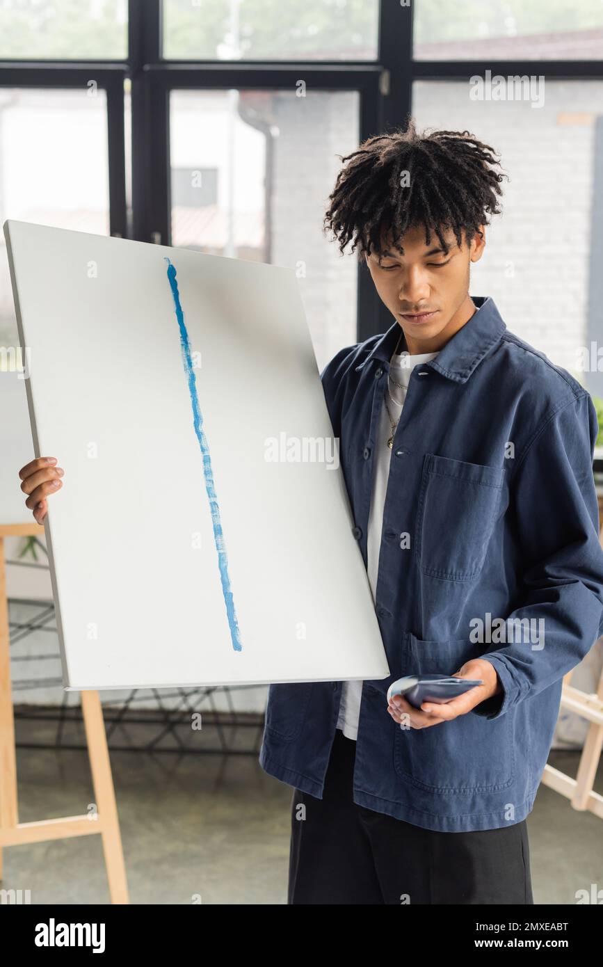 Young african american artist holding canvas and paint in studio,stock image Stock Photo