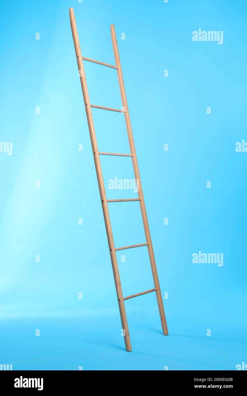 Modern wooden ladder on light blue background Stock Photo - Alamy